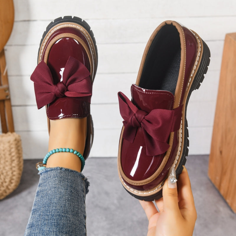 Mocasines con lazo burdeos y acabado brillante, suela gruesa con ribete claro.