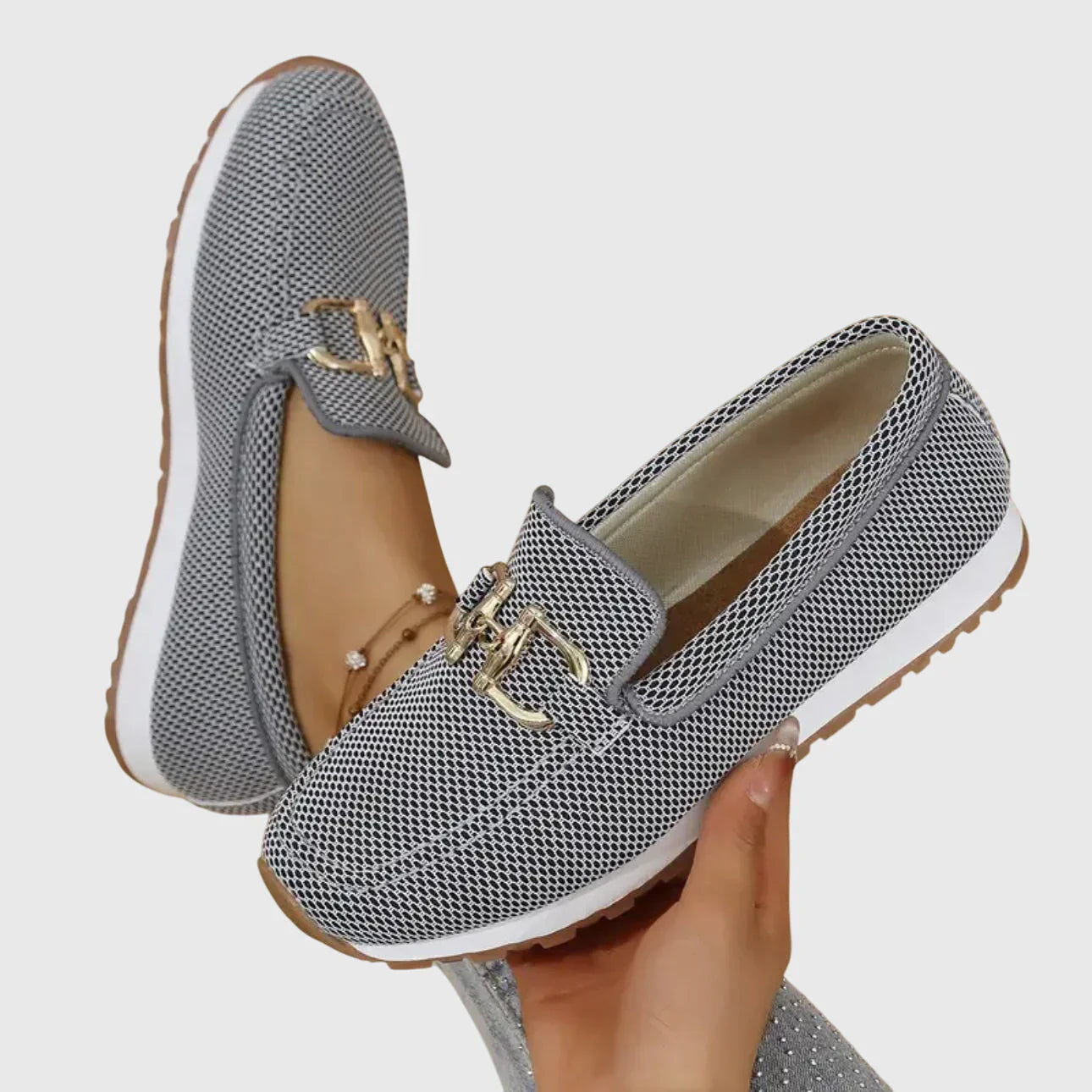 Zapatillas tipo mocasín Chiara grises con detalle metálico dorado y suela beige.