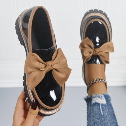 Mocasines con lazo beige y acabado negro, suela gruesa con costuras claras.