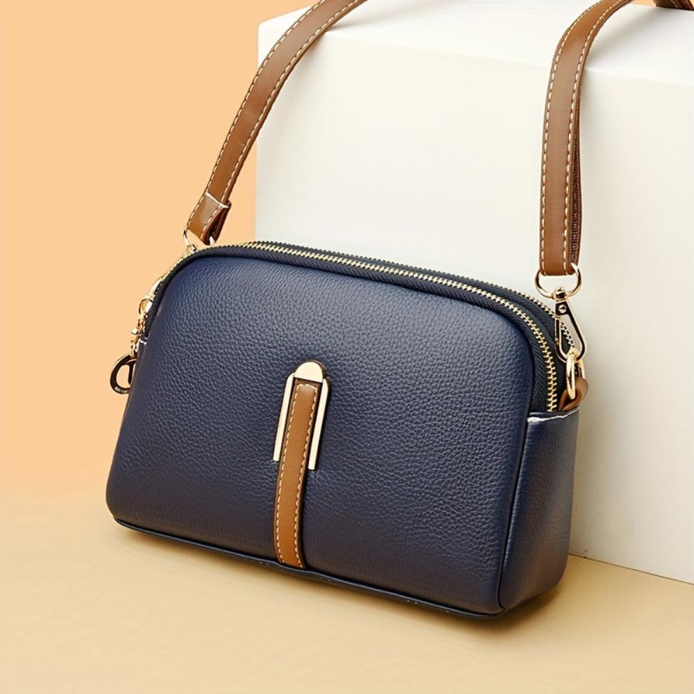 Bolso de hombro azul oscuro con textura de lichi, correa marrón y cierre cremallera.