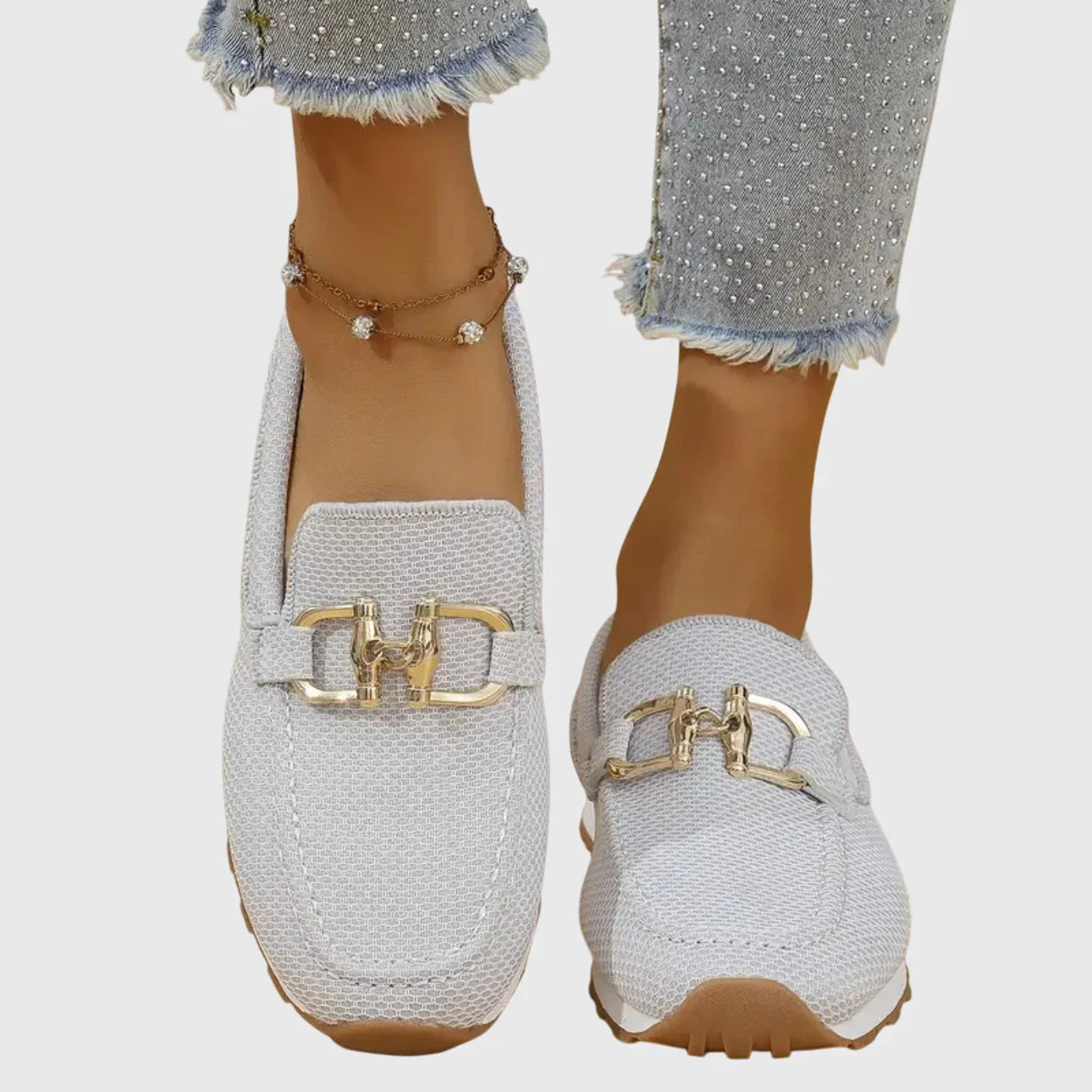 Zapatillas tipo mocasín Chiara blancas con adorno metálico dorado y suela marrón.