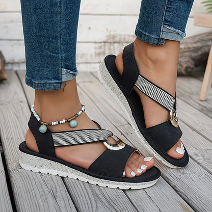 Sandalias planas negras con hebilla metálica dorada y pulsera de cuentas turquesa