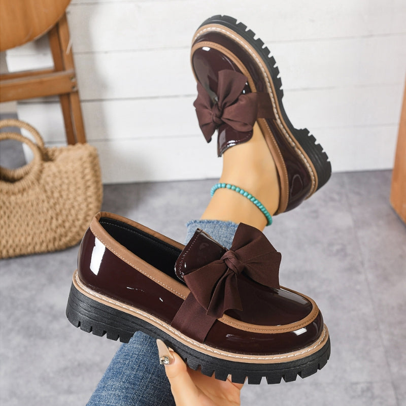 Mocasines con lazo marrón oscuro, empeine tipo charol y suela gruesa dentada.