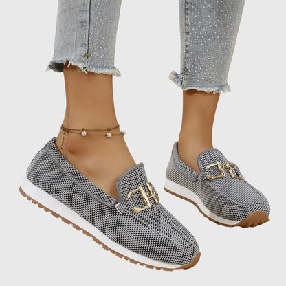 Zapatillas tipo mocasín Chiara grises con detalle metálico dorado y suela beige.