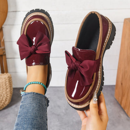 Mocasines con lazo burdeos y acabado brillante, suela gruesa con ribete claro.