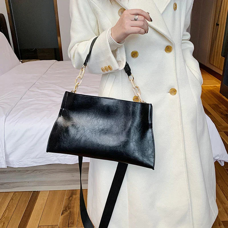 Bolso de hombro de cuero negro con asa superior y correa dorada
