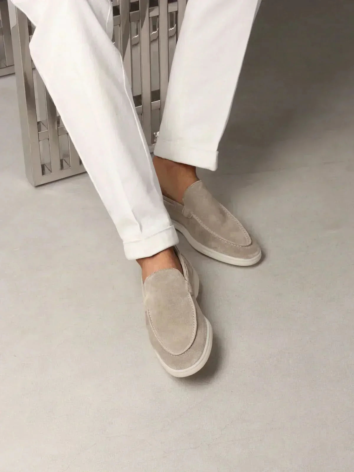Mocasines de ante color beige, estilo slip-on, con pantalón blanco visible y suela clara.