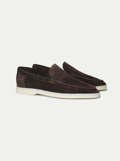 Mocasines de ante café oscuro, slip-on, con suela blanca.