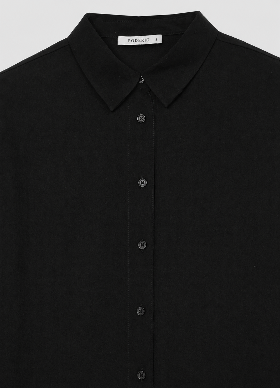Camisa negra lisa: cuello y botonera con botones discretos.