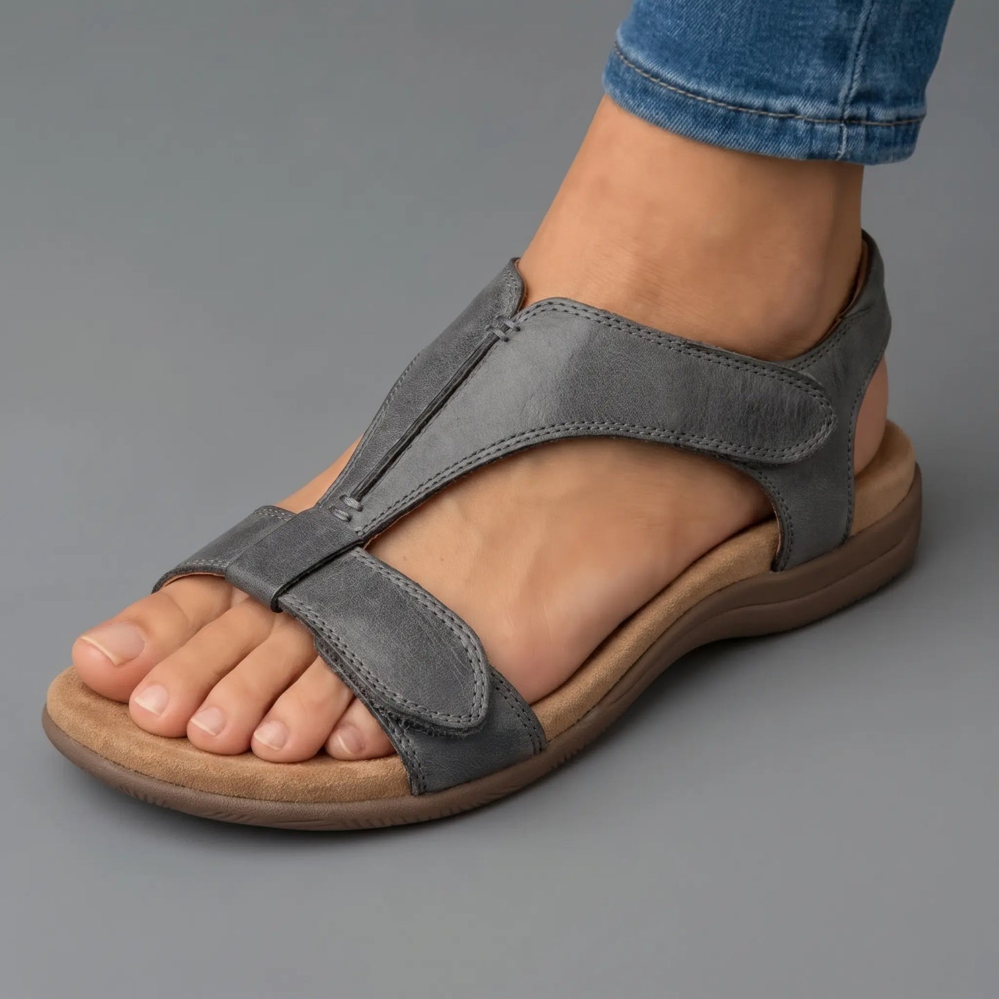Sandalias ortopédicas grises de piel con tira ajustable al tobillo y suela amortiguada.