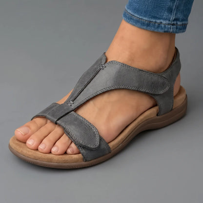 Sandalias ortopédicas grises de piel con tira ajustable al tobillo y suela amortiguada.
